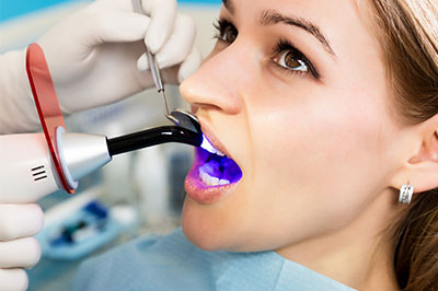 Woman receiving dental implant with device, surrounded by medical equipment and staff.