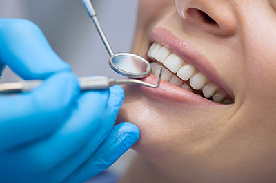 The image shows a person receiving dental care, with a dental hygienist using a dental tool on their teeth while wearing protective gloves and a face mask.