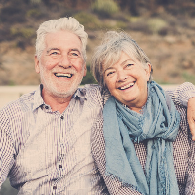 The image features a woman with a broad smile, leaning on her hand near her shoulder, posing for a portrait against a neutral background.