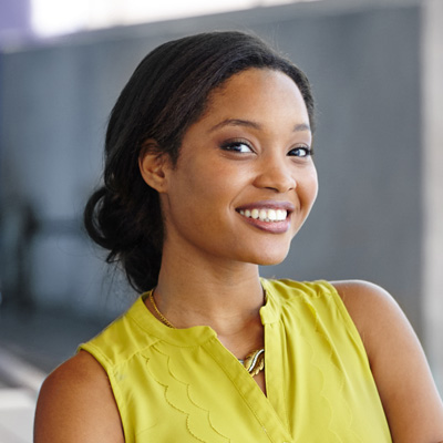 A woman with a radiant smile, wearing a yellow top, poses confidently against a blurred background.