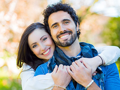 A man and woman are hugging each other, smiling, with the man wearing a bandana around his neck.