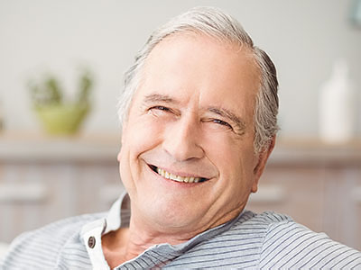 The image shows a man with white hair smiling at the camera while sitting comfortably in a chair.