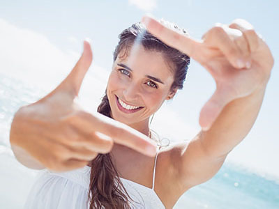 A woman with long hair is smiling at the camera while holding up her hand with fingers spread apart.