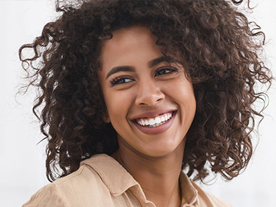 The image features a smiling woman with curly hair, wearing a light-colored top, against a white background.